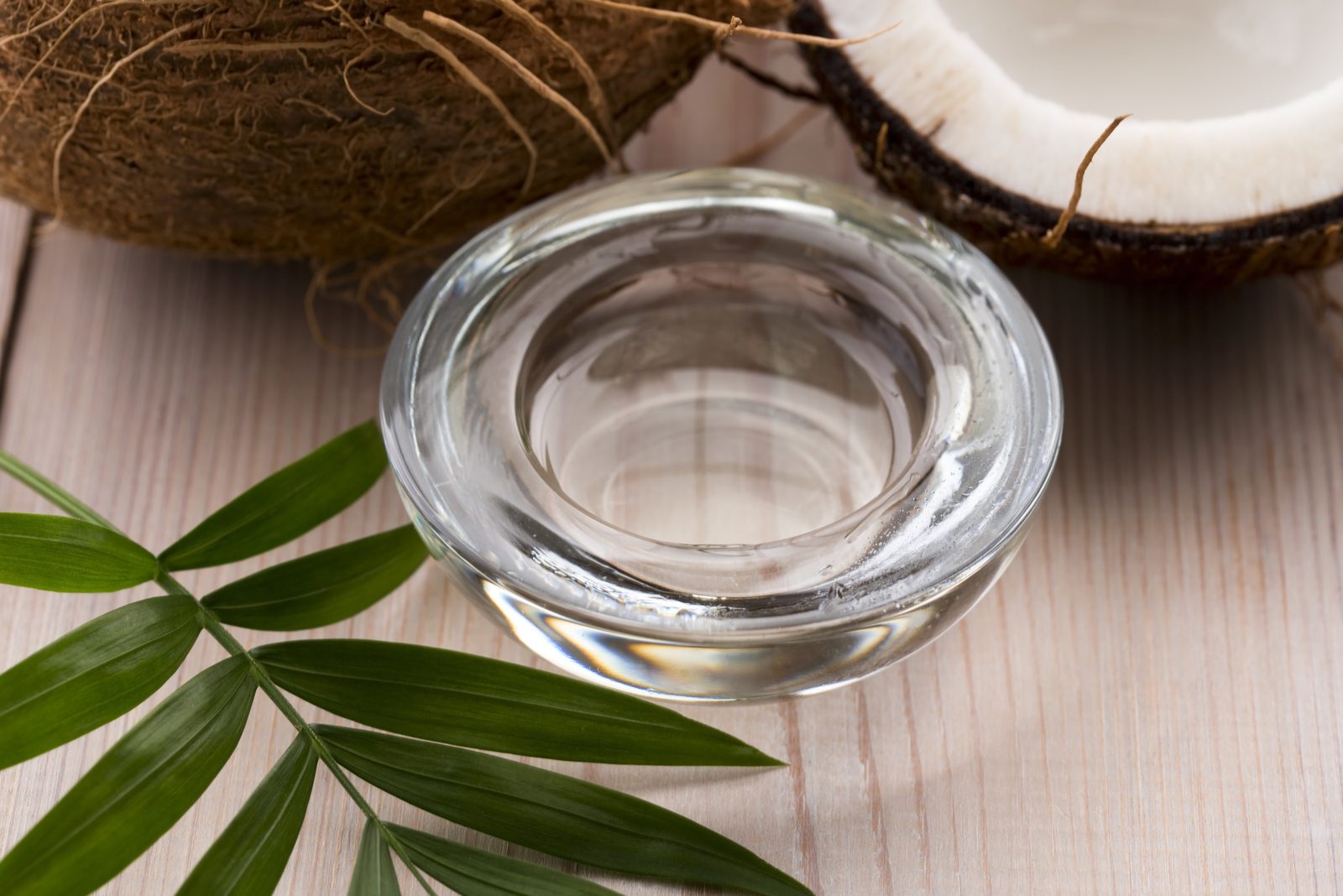 clear oil in a glass bowl next to coconut halves